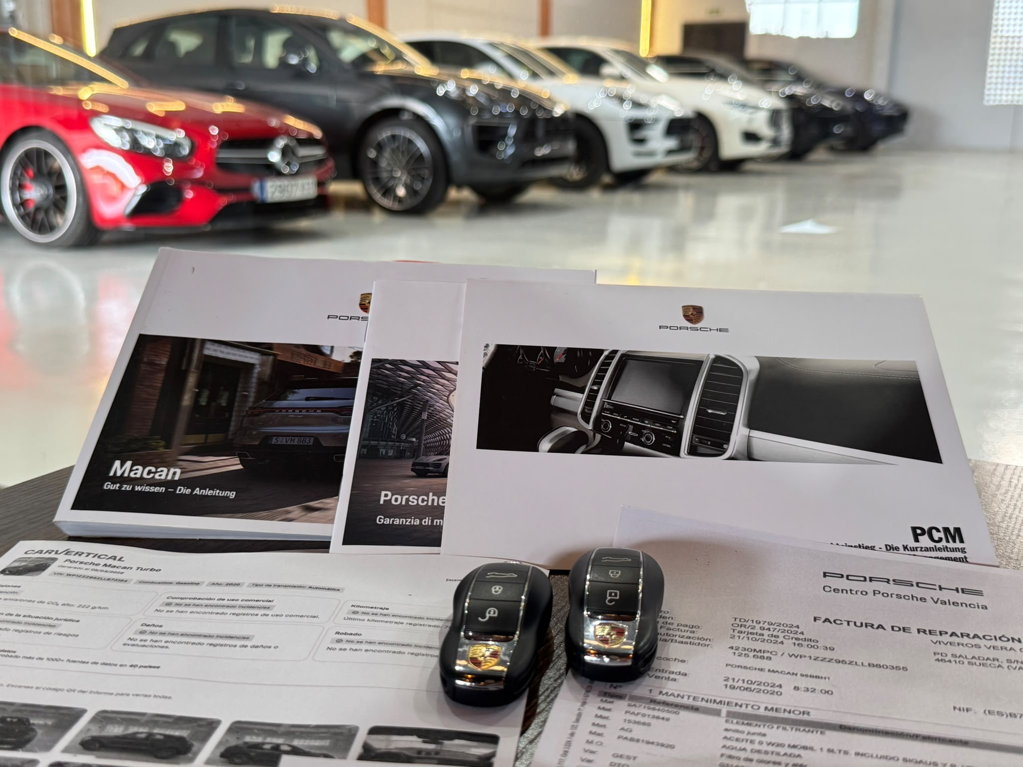 Documentación y llaves de un Porsche con varios vehículos seleccionados al fondo