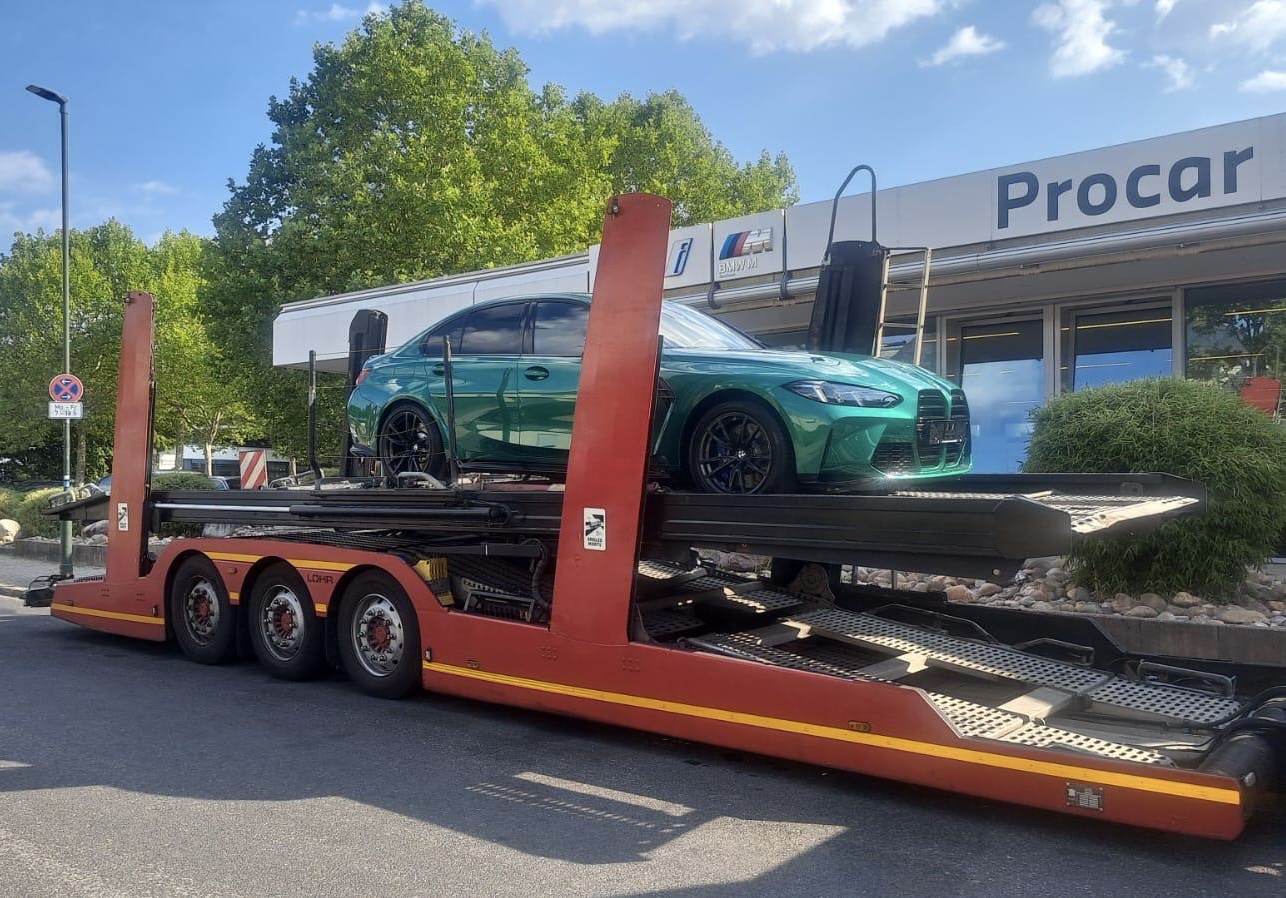 BMW verde cargado en un portacoches frente a las instalaciones de origen