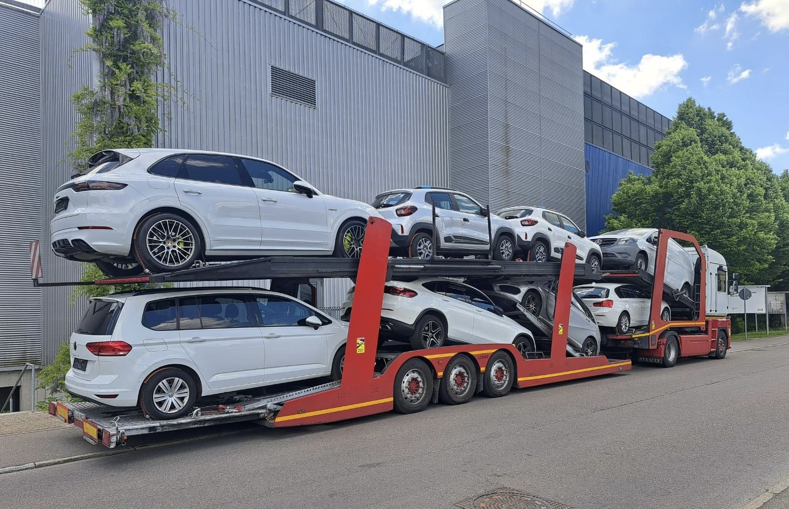 Portacoches cargado con varios vehículos junto a una nave industrial